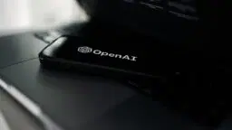 A smartphone displaying the OpenAI logo rests on a laptop keyboard.